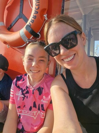Andrea in sunglasses taking a sunny selfie with her daughter in a pink sports top on a day out