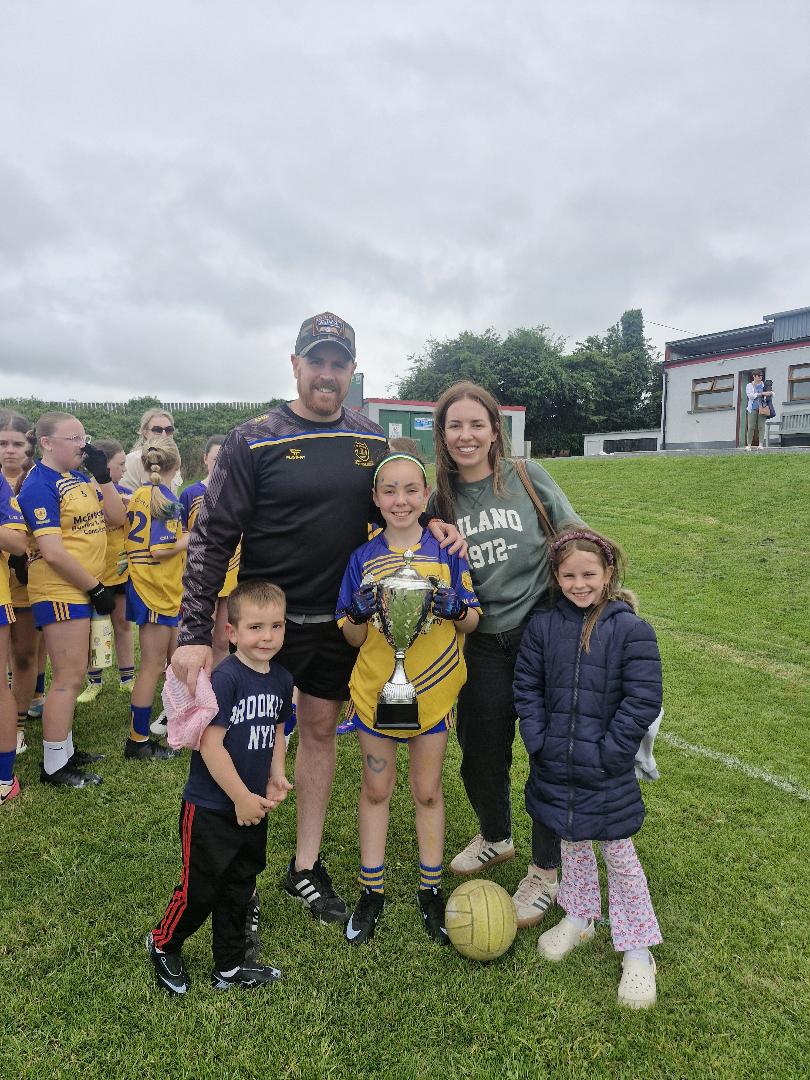 Andrea, her partner and their three children on a football pitch, her daughter holding a silver trophy after a team win