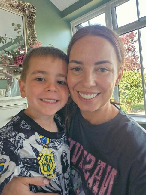 Andrea cheek to cheek with her young son, both smiling at home